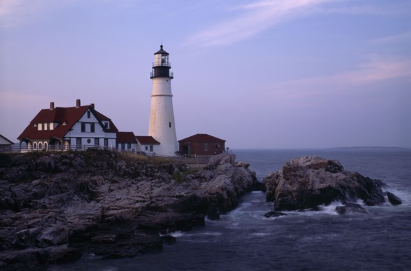 USA, Maine, Portland, Portland Head Lighthouse. Waves crashing against rocks seen at dusk in warm