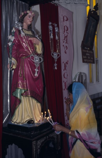 INDIA, Karnataka, Mysore, Indian woman lighting candles in front of statue of religious figure at