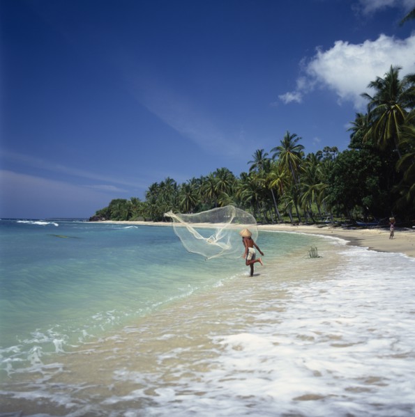INDONESIA, Lombok, Mentiggi, Fisherman casting fishing net into sea from the surf on a coconut palm