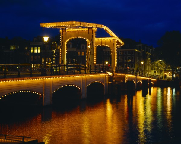 HOLLAND, North, Amsterdam, Magere Brug or Skinny Bridge illuminated at night with lights reflected