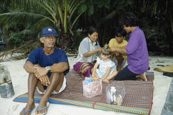 THAILAND, South, Koh Samui, Young Western girl on sandy beach having her hair braided by three Thai