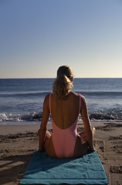 USA, Florida , Sunbathing, Young woman sitting on a sandy beach wearing a pink swimsuit with back