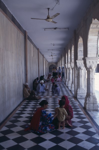 INDIA, Delhi, "Sikh pilgrims sitting on long, colonnaded temple passage-way with black and white