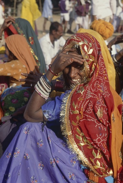 INDIA, Rajasthan, Pushkar, Seated smiling Rajasthani woman in colourful sari looking over her