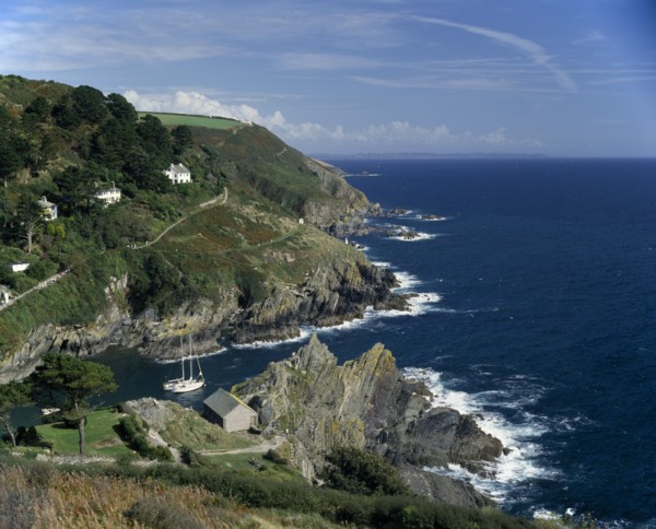 ENGLAND, Cornwall, South Cornwall . Rugged coastline with yachts in bay and houses on hillside