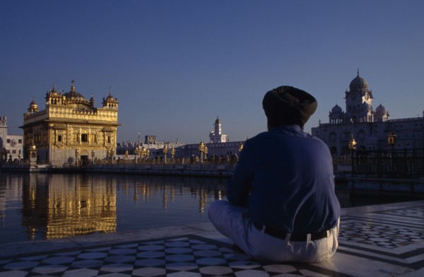 INDIA, Punjab, Amritsar, Golden Temple with pilgrim sat beside sacred pool in the foreground.