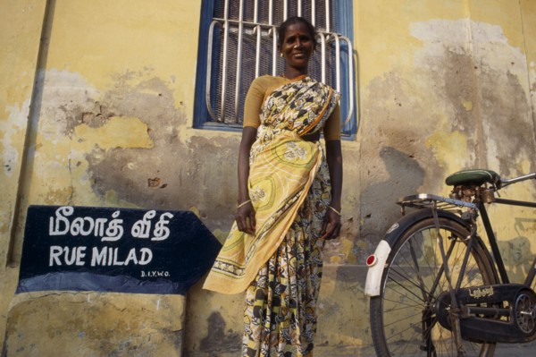 INDIA, Tamil Nadu, Pondicherry, Woman in a yellow sari standing in front of a yellow wall beside a