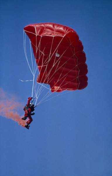 20003695 SPORT Air Parachuting Parachutist with red garments  red Parachute and with red smoke coming from his boots.
