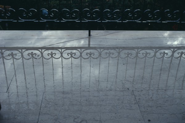 GREECE, Reflection, Decorative wrought iron balcony railings casting a shadow onto a pale wet floor