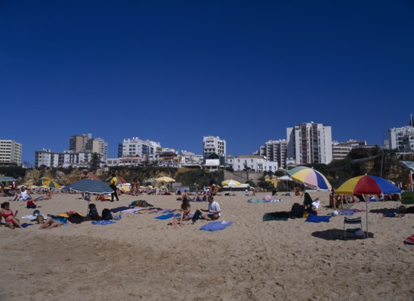PORTUGAL, Algarve, Praia da Rocha, View of beach with people sunbathing and clifftop hotels behind