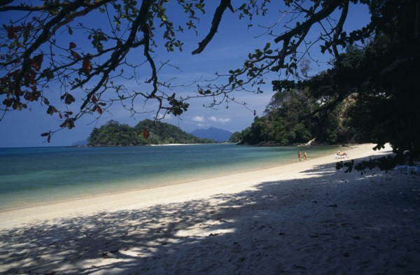 MALAYSIA, Kedah, Langkawi, Datai Bay beach with tourists walking by the water’s edge looking out to