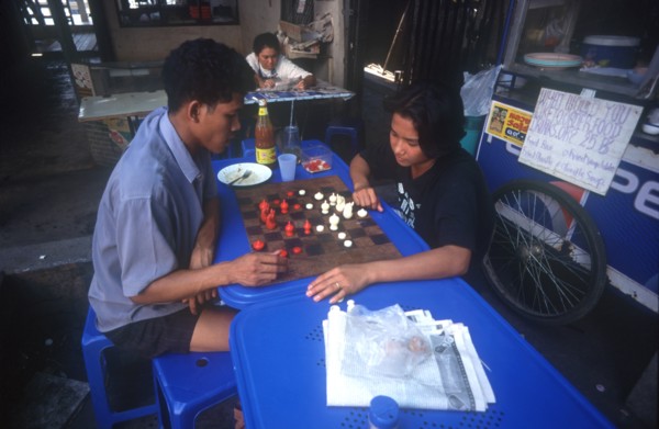 THAILAND, Bangkok, Couple playing a board game at a streetside cafe.