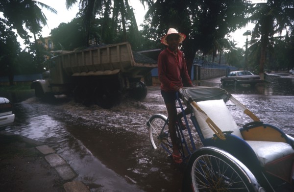 CAMBODIA, Phnom Pehn, Rickshaw and truck driving through a flooded street near the Royal Hotel