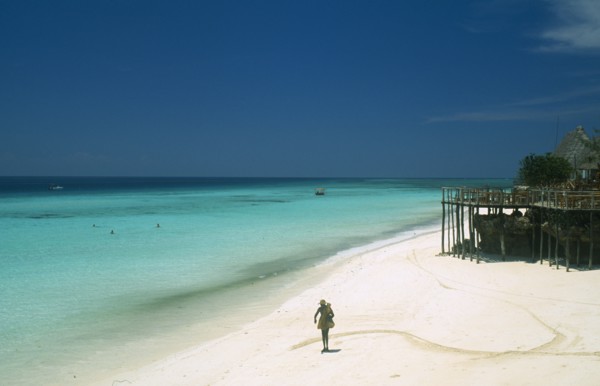 TANZANIA, Zanzibar Island, "Nungwi.  Single figure walking along sandy beach beside aquamarine