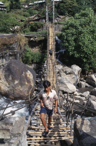 NEPAL, Annapurna Region, Marsyangdi River, Near Besisahar.  Young man crossing wood and rope foot