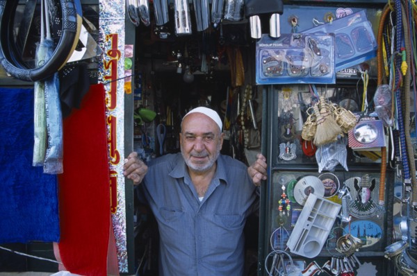 SYRIA, North, Halab, Male shopkeeper at the entrance to his shop with display of mixed goods