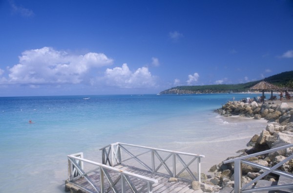 WEST INDIES, Antigua, Dickenson Bay, Raised area of sand fortified by rocks with people sitting on