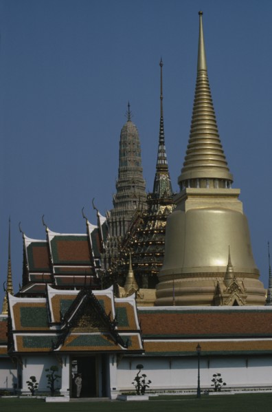 THAILAND, Bangkok, Grand Palace, Aka Wat Phra Kaeo. Exterior view of golden spires and man on guard