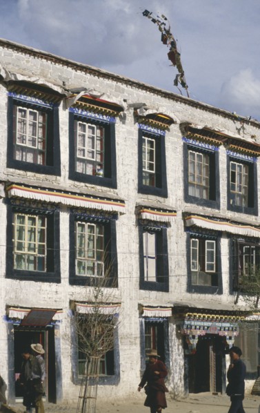 CHINA, Tibet, Lhasa, Traditional houses with ribbons hanging above the windows and people walking