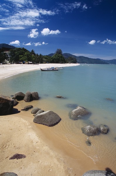 MALAYSIA, Penang, Batu Ferringhi, View along shore of quiet sandy beach with moored boat in middle