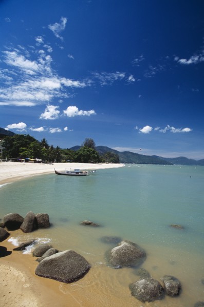 MALAYSIA, Penang, Batu Ferringhi, View along shore of quiet sandy beach with moored boat in middle