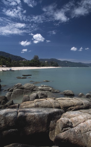 MALAYSIA, Penang, Batu Ferringhi, View over rocks and bay of turquoise water towards distant moored