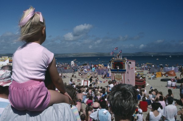 ENGLAND, Dorset , Weymouth, View over crowds on the beach viewing Punch and Judy show with girl in