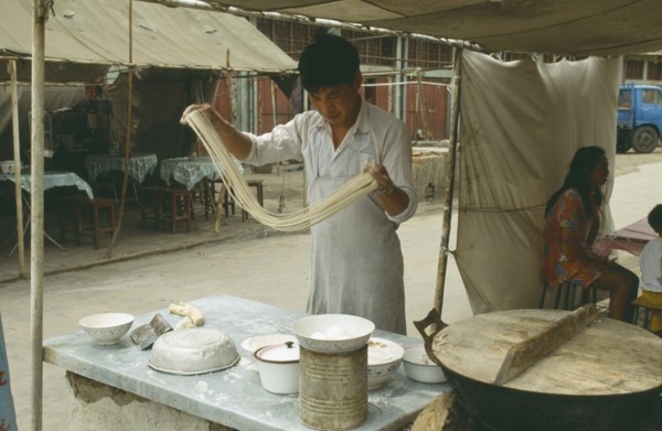 CHINA, Henan Province, Shaolin Monastery, Young man making noodles at food stall by swinging the