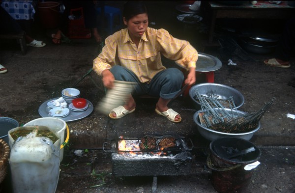 VIETNAM, Hanoi, Woman cooking at curb side food stand.