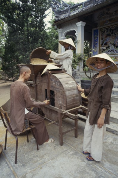 VIETNAM, Hue, Monks husking rice in a traditional hand driven machine