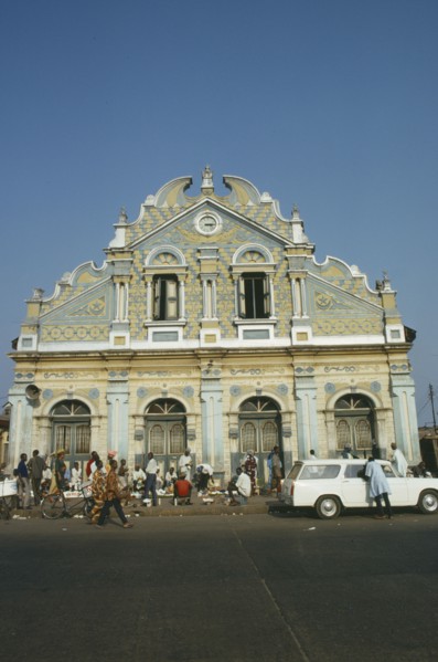 NIGERIA, Lagos, Street scene with roadside vendors ad passers by in front of mosque with pale blue