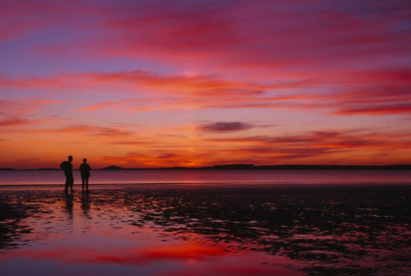 IRELAND, Sligo, Rosses Point, Two figures silhouetted on the beach watching dramatic deep pink and