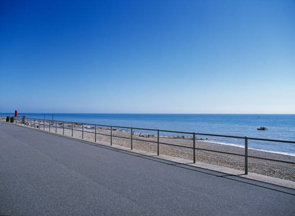 20059214 ENGLAND East Sussex Bexhill on Sea View from path across railings towards shingle beach and calm blue sea.