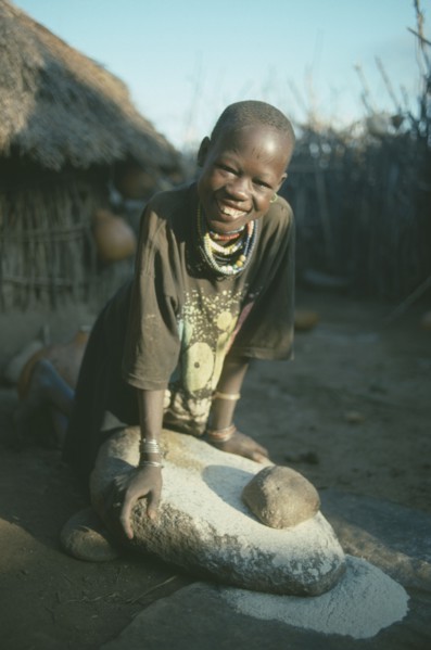 UGANDA, Karamoja, Tribal Poeple, Dodoth Karamojong girl grinding millet on stone.