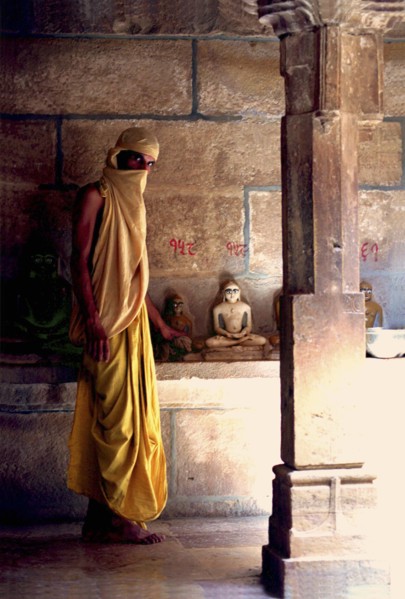 INDIA, Rajasthan, Mt Abu, Fly monk standing near Buddha statues with a scarf covering his head and