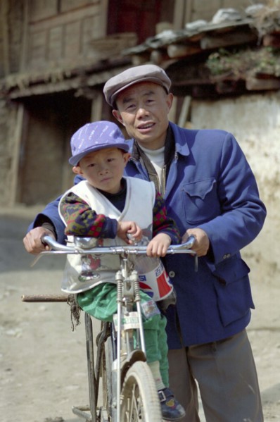 CHINA, Yunnan, Lijiang, Portrait of a man standing with a small boy on his bike holding a Pepsi