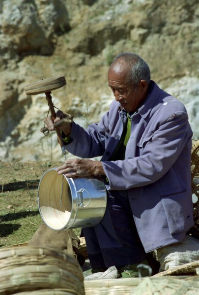 CHINA, Yunnan, Shapin, Man using old style drilling tool on metal and wooden pot