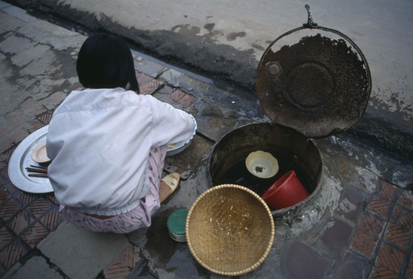 VIETNAM, North, Hanoi, Girl washing pots in a communal water well in the pavement  beside a drain