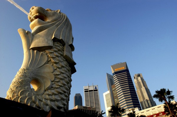 SINGAPORE, Merlion, Merlion statue spouting water in evening light with city skyscrapers beyond