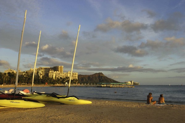 USA, Hawaii, Honolulu, Diamond Head. Sandy beach with two people sitting near boats on the sand in