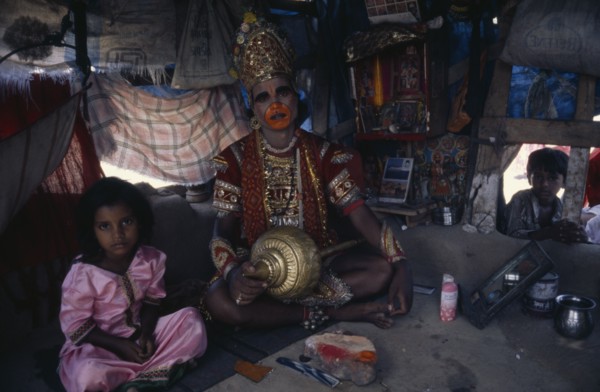 INDIA, Gujarat, Bhavnagar, Man in his shanty house dressed up as the Hindu deity Hanuman.  Child