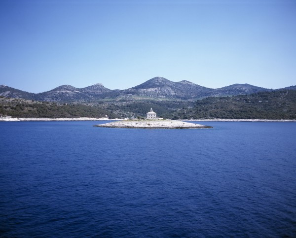 CROATIA, Dalmatia, View over water toward small islet between Sibenik and Trogir with lighthouse in