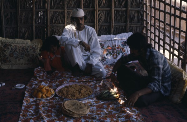 OMAN, Food, Two men and girl sitting with a meal served in communal dishes in front of them.