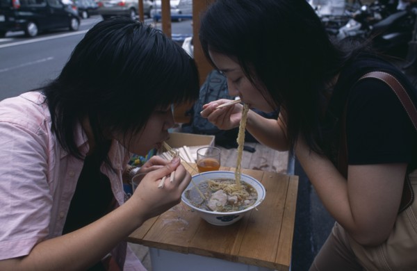JAPAN, Honshu, Tokyo, Tsukiji Fish Market. Two girls sharing a bowl of noodles at a street stall