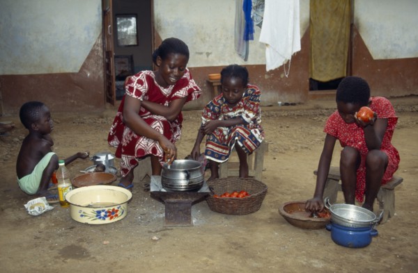 GHANA, Cooking, Woman with children cooking Abenkwan or palm nut soup a thick broth made from the