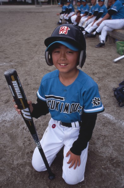 JAPAN, Honshu, Tono, Young boy kneeling on the grass wearing a Baseball kit holding a bat