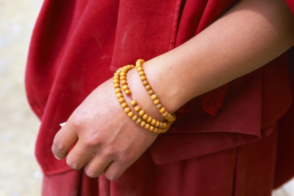 TIBET, Shigatse, Detail of a monks hand with a rosary wrapped around his wrist wearing a red robe.