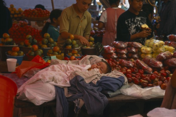 MEXICO, Oaxaca, Sleeping child on market stall selling fruit.