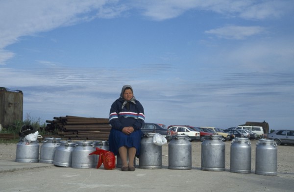 ESTONIA, Baltic Coast, Woman sitting on milk cans waiting for ferry.