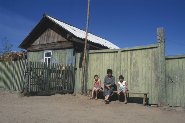 RUSSIA, Siberia, Lake Baikal, Buryat woman and children outside painted wooden fence of house.  The